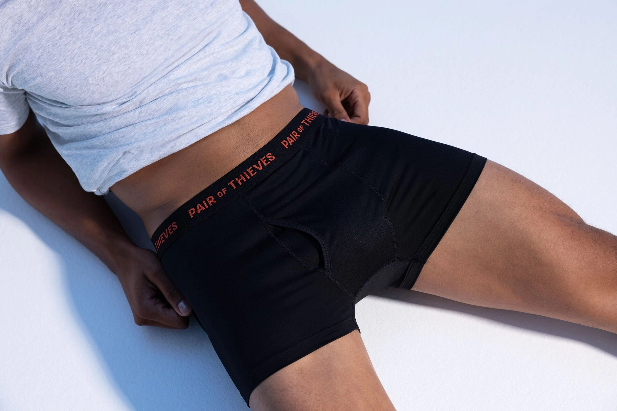 Model in black boxer briefs and a white tee against a pale blue backdrop